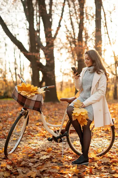 Krásná Šťastná Žena Kabátě Sedí Kole Pomocí Smartphonu Podzimním Parku — Stock fotografie