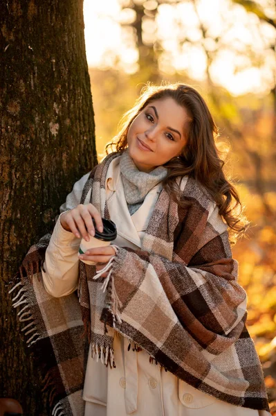 站在树下喝咖啡的金发女人笑着 美丽的年轻女士在秋天的公园里感到快乐 — 图库照片