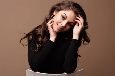 Güzel gülümseyen genç Avrupalı kadın portresi. Kameraya bakan siyah kazaklı, güzel yüzlü ve saçlı bir kız. Kahverengi arka planda izole edilmiş. Boşluğu kopyala