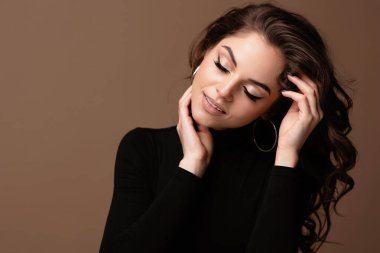 Çekici, rüya gibi genç Avrupalı kadın portresi. Kız siyah kazak giyer, gözleri kapalıdır ve sandalyeye oturur. Kahverengi arka planda izole edilmiş. Boşluğu kopyala