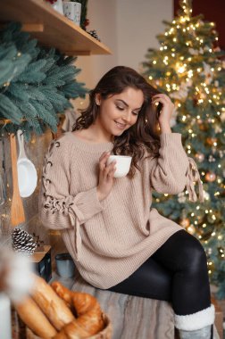 Kahvesini içen ve Noel boyunca mutfak tezgahında oturan esmer kadının dikey görüntüsü. Tatil kavramı 