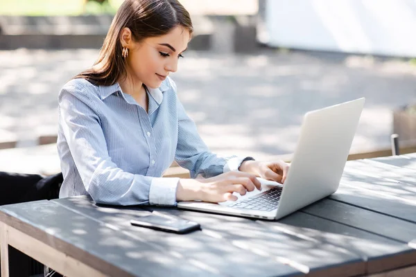 Avrupalı iş kadını dışarıda dizüstü bilgisayarda daktilo kullanıyor. Güneşli parktaki masada oturan güzel bir genç kız. Modern kadın yaşam tarzı. Uzak ve serbest çalışma kavramı