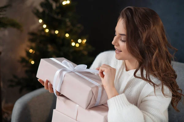 坐在圣诞树旁的沙发上 一头卷曲的头发 把蝴蝶结绑在礼品盒旁 喜形于色 新年概念 — 图库照片
