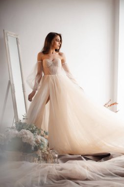 Gelinin sabahının romantik atmosferi. Şampanyanın renginde gelinlik giymiş nazik gelin pencereden dışarı bakar. 