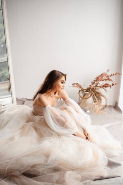 Vertical view of the bride in wedding dress is sitting in front of the window. Romantic atmosphere of the bride's morning concept 
