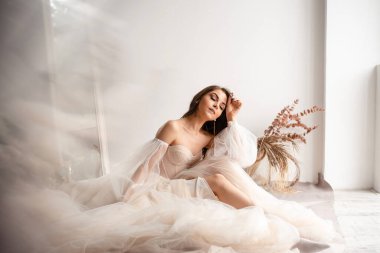 Şampanyalı esmer gelinin, lüks gelinlik içinde, stüdyo içinde kameranın önünde kapalı gözlerle poz verirken geniş açılı görüntüsü.