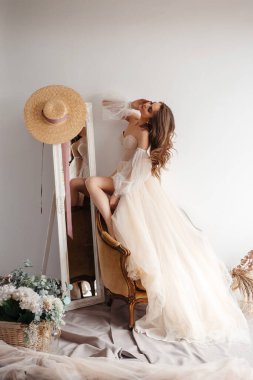 Beautiful dress. Full length of attractive young woman wearing wedding dress standing at the armchair near the mirror in bridal shop. Stock photo 