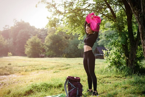 ヨーロッパのアスリートの女の子は森の近くの緑の草原でピンクのジャケットを脱ぐ 目を閉じた若い美しい笑顔の女性は スポーツウェアを着用 自然の中で休息と観光の概念 晴れた日 — ストック写真
