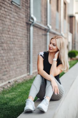 Spor kıyafetler giyen aktif genç bir kadın ve temiz havada bisiklet sürdükten sonra bileğinde dinlenen akıllı bir saat. Sağlıklı ve zinde bir sarışın şehirde oturuyor ve aşağıya bakıyor..