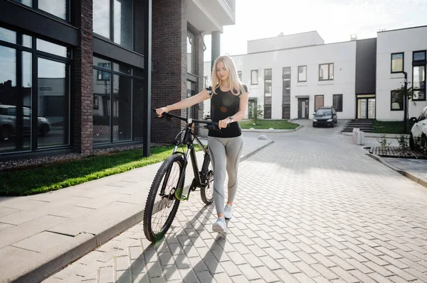 手に黒い自転車で通りを歩くスポーツ服の白人女性選手 若いです女性ブロンド準備のために朝サイクリング上の新鮮な空気 — ストック写真