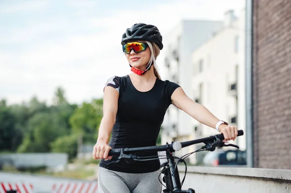 黒い自転車で屋外を歩く細い体を持つ若い白人女性 スポーツ服 安全ヘルメットとミラーガラスを身に着けているアクティブな女性のブロンド サイクリングのコンセプト — ストック写真