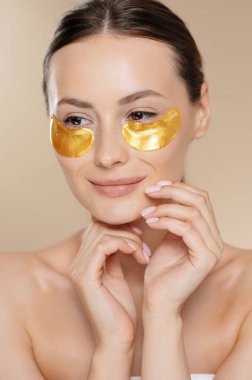 Stüdyoda güzel, sağlıklı ciltli, gözlerinin altında güzellikler olan bir manken. Beyaz kadın, yüz kırışıklıklarını azaltmak için profesyonel kozmetik kullanıyor..