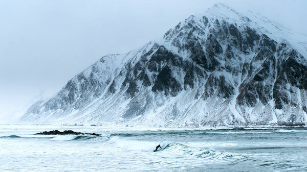 Surfing on picturesque arctic beach Unstad on Lofoten islands in Norway, the iconic travel destination for surfers of all over the world. Location - Norwegian sea coastline, Scandinavia, Europe.
