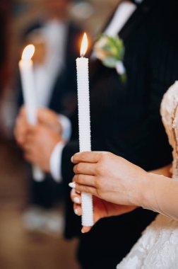 Kilise töreninde ellerinde mum tutan düğün çifti, yakın plan.
