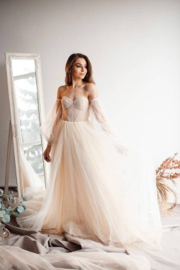 Aynanın yanında poz veren güzel gelinin uzun bir görüntüsü. Nazik gelin törene gidiyor. Profesyonel fotoğraf stüdyosu konseptinde fotoğraf çekimi. 