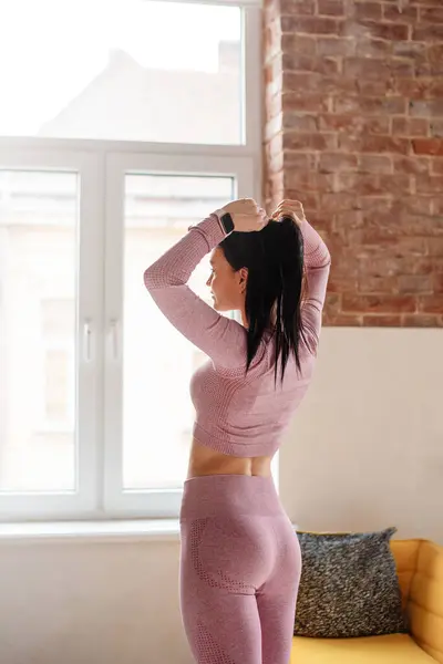 Spor yaparken evinde dinlenen atletik vücutlu genç bir kadının arka görünüşü. Siyah saçlı beyaz kadın şık spor kıyafetler giyiyor..