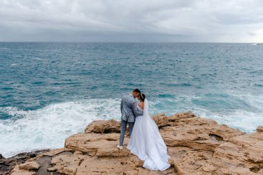 Yeni evliler deniz kenarındaki kayalıklarda nazikçe sarılıyorlar ve Kıbrıs 'ın doğasının tadını çıkarıyorlar. Dikiz aynası. Yeni evlilerin balayı..