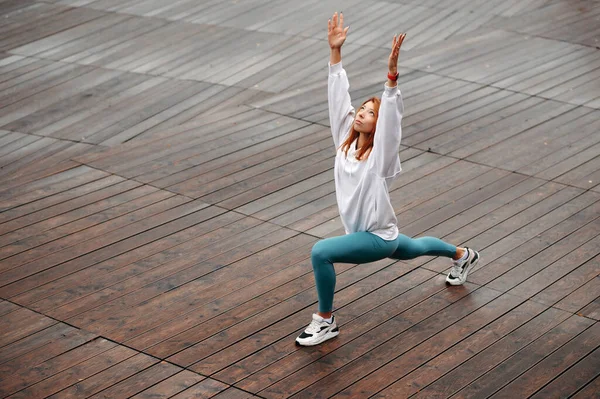 Ahşap iskelede spor yapan kızıl saçlı aktif genç bir kadın. Soğuk sonbahar zamanı dışarıda antrenman yapmak.