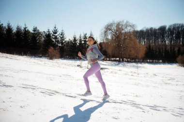Tüylü at kuyruklu, kar yağışı içinde koşan, motive olmuş ve aktif, genç bir kızın yan görünüşü.