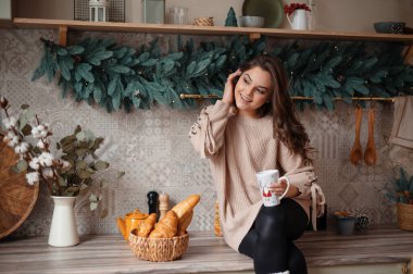 Memleketteki dekore edilmiş mutfakta gülümseyen ve içecek içen olumlu bir kadın. Tatil kavramı 