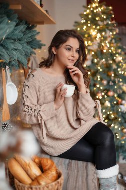 Kahvesini içen ve Noel boyunca mutfak tezgahında oturan esmer kadının dikey görüntüsü. Tatil kavramı 