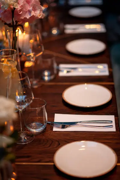 Wedding or dinner table setting with plates and cutlery on wooden table with warm candles light