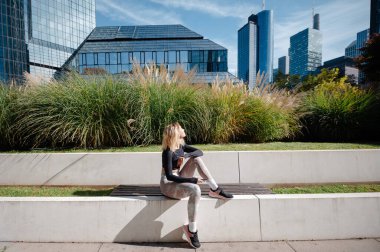 Moda spor kıyafetleri içinde sarışın bir kız sokakta spor salonu egzersizi yaptıktan sonra poz veriyor. Açık hava sporları, şehir tarzı ve sağlıklı yaşam tarzı konsepti 