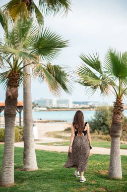 Kıbrıs 'ta lüks egzotik tatil beldelerinin bulunduğu bir bölgede palmiye ağacının yanında çimlerde yürüyen beyaz bir kadın. Yaz zamanı, keyif ve rahatlama kavramı.