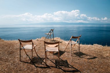 Kayaların kenarındaki dört boş tabure, Yunanistan 'da mavi gökyüzü ve denizin arka planına karşı duruyor