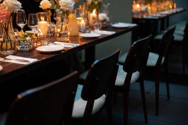 Loş bir restoranda mum ve çiçeklerle süslenmiş şık bir yemek masası..