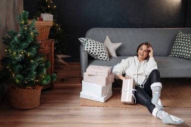Pozitif kadın Noel 'den sonraki sabah seviniyor. Kadın Noel ağacının arka planında oturma odasında oturuyor. 