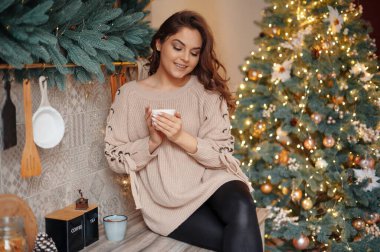 Memleketteki dekore edilmiş mutfakta gülümseyen ve içecek içen olumlu bir kadın. Tatil kavramı 