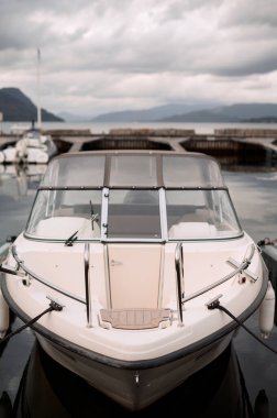 Arka planda bulutlu bir gökyüzü olan beyaz bir motorlu tekne marinaya yanaştı..