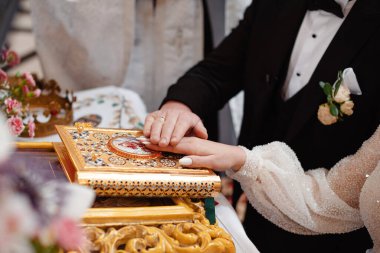Bir çift, evlilik töreninde birlik ve bağlılığı sembolize eden dekoratif bir dini kitaba dokunuyor. Olay yeri çiçeklerle ve süslü detaylarla süslenmiş..