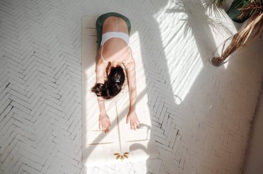 Güneşli bir odada, çocuk pozunda yoga yapan bir kadın..