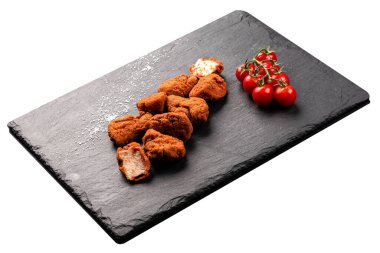 Yanında bir yığın taze vişneli domates ile birlikte siyah bir tabakta kızarmış tavuk parçaları servis ediliyor. Tabak bir tutam tuz ile süslenir, tavuğun dokusunu ön plana çıkarır..