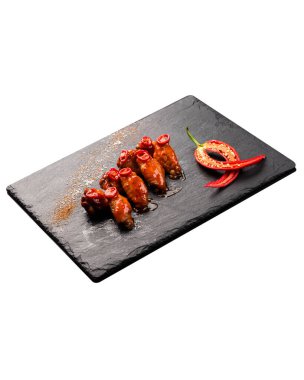 Dilimlenmiş kırmızı biberle süslenmiş baharatlı tavuk kanatları siyah bir tabakta..