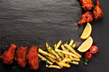 Kızarmış tavuk kanadı, patates kızartması, limon ve vişneli domates tabağı..