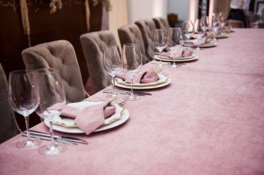 Pembe masa örtüsü, tabaklar ve cam süslemeli zarif bir yemek masası. Özenle düzenlenmiş çatal bıçak ve peçetelerle özel bir durum için sofistike bir ortam yaratıyor..