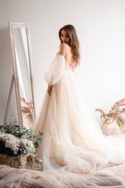 Aynanın yanında poz veren güzel gelinin uzun bir görüntüsü. Nazik gelin törene gidiyor. Profesyonel fotoğraf stüdyosu konseptinde fotoğraf çekimi. 
