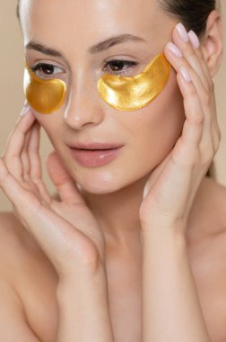 Stüdyoda güzel, sağlıklı ciltli, gözlerinin altında güzellikler olan bir manken. Beyaz kadın, yüz kırışıklıklarını azaltmak için profesyonel kozmetik kullanıyor..