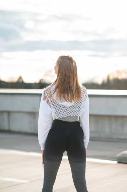 Atletik giysili bir kadın açık havada, parlak bir gökyüzü ile yüz yüze duruyor..