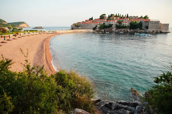 Kumlu bir sahil kasabası manzarası ve sakin deniz, yemyeşil ve tarihi binalarla çevrili..