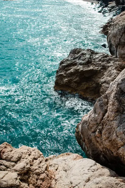 Turkuvaz deniz dalgalarıyla kayalıklara çarpan kayalık kıyı şeridi..