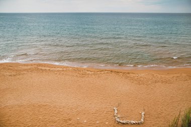 Sakin bir sahil sahnesi, bulutlu bir gökyüzünün altında kumlu sahilde hafif dalgalar çakıyor..