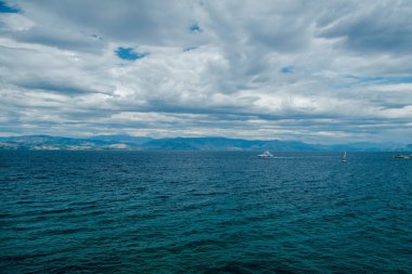 Uçsuz bucaksız mavi bir okyanusta, bulutlu bir gökyüzünün altında yatı ve yelkenlisi olan sakin bir deniz manzarası..