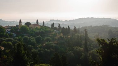 Şafak vakti dingin bir Toskana kırsalı manzarası. Yuvarlanan tepeler, zeytin ağaçları ve uzak bir köy..