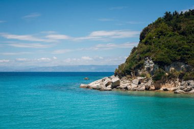 Turkuaz suları ve berrak mavi gökyüzünün altında kayalık bir uçurumu olan sakin bir kıyı manzarası..