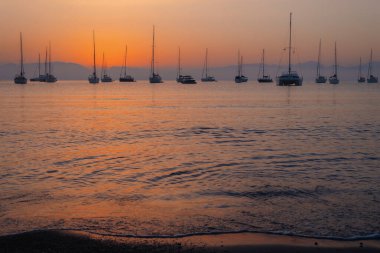 Sakin bir denizin üzerinde sakin bir gün batımı ufukta siluetli yelkenliler.