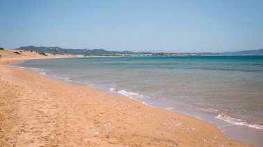 Yumuşak dalgaları ve berrak mavi gökyüzü ile sakin bir sahil manzarası sunan sakin kumlu bir sahil..